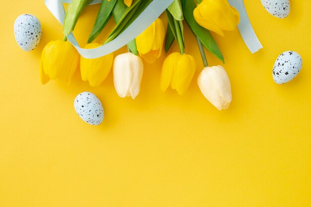 Composición de Pascua hecha con tulipanes y huevos pascuales sobre fondo amarillo con espacio de copia