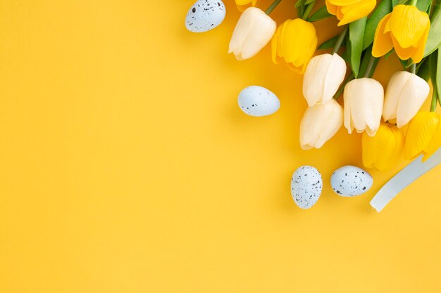 Composición de Pascua hecha con tulipanes y huevos pascuales sobre fondo amarillo con espacio de copia