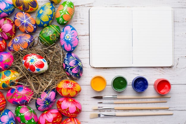 Composición de pascua con huevos, cuaderno y tarros de pintura