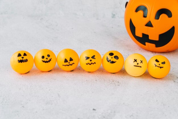 Composición con pequeña bola naranja con caras espeluznantes en fila