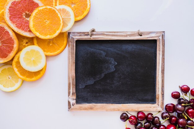 Composición con pizarra, rodajas de naranjas y cerezas