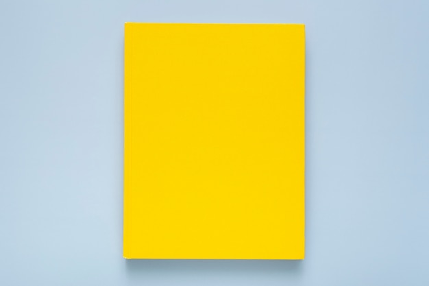 Composición plana con cuaderno amarillo sobre fondo azul.