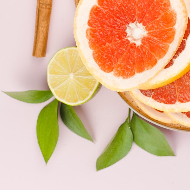 Composición de rodajas de pomelo con lima y hojas verdes cerca de canela