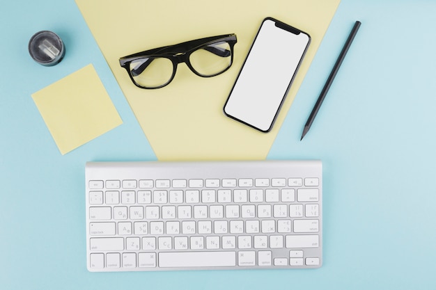 Composición de smartphone, teclado, gafas y lápiz.