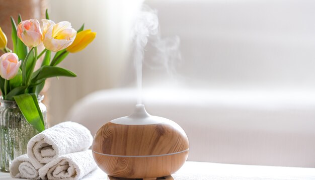 Composición de spa con aroma de moderno difusor de aceite con productos para el cuidado corporal. Toallas blancas retorcidas, verdes primaverales y flores. Concepto de spa para el cuerpo y la salud.