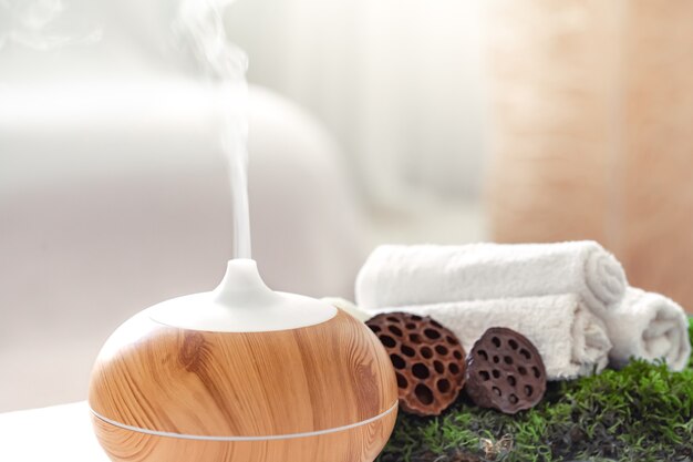 Composición de spa con aroma de moderno difusor de aceite con productos para el cuidado corporal. Toallas blancas retorcidas, verdes primaverales y flores. Concepto de spa para el cuerpo y la salud.