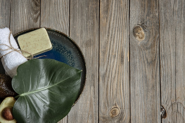 Composición de spa con jabón, aguacate, toalla y hojas en el espacio de copia de superficie de madera.