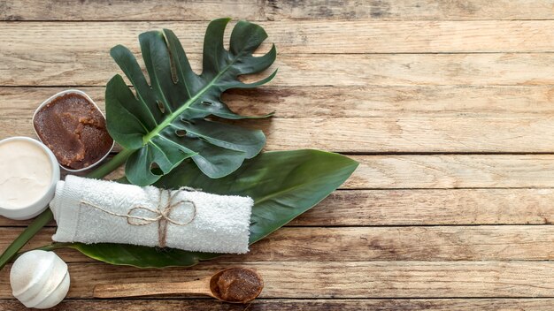 Composición de spa con toallas y hojas tropicales en una pared de madera.