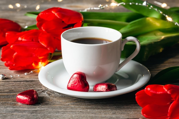 Composición con una taza de dulces en forma de corazón de café y primer plano de flores rojas