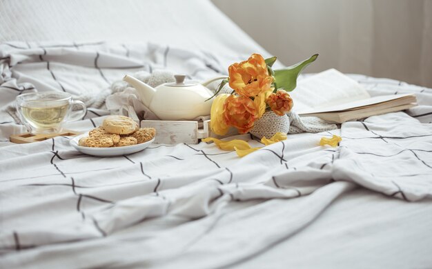 Composición con una taza de té, una tetera, un ramo de tulipanes y galletas en la cama