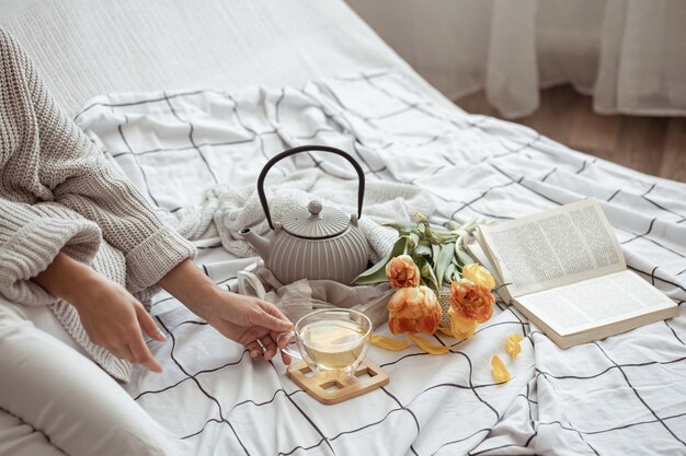 Composición con una taza de té, una tetera, un ramo de tulipanes y un libro en la cama