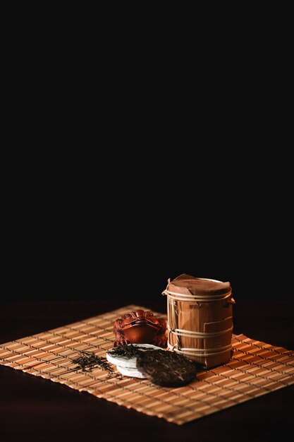 La composición del té del puer con el sapo de oro en una estera de bambú. Fondo negro.