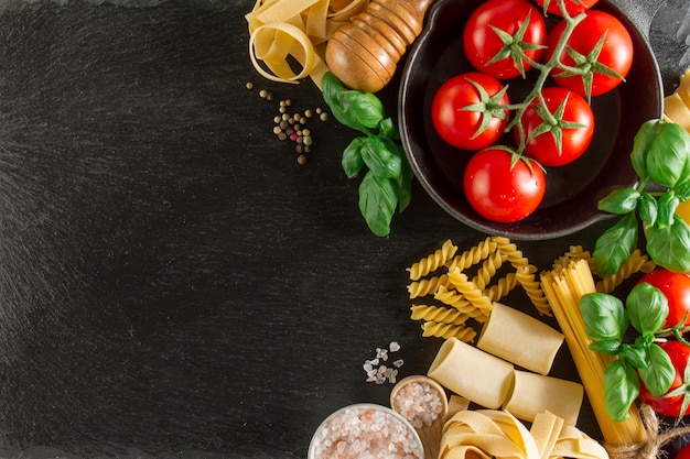 Composición con variedad de pasta, tomates y albahaca sobre superficie oscura