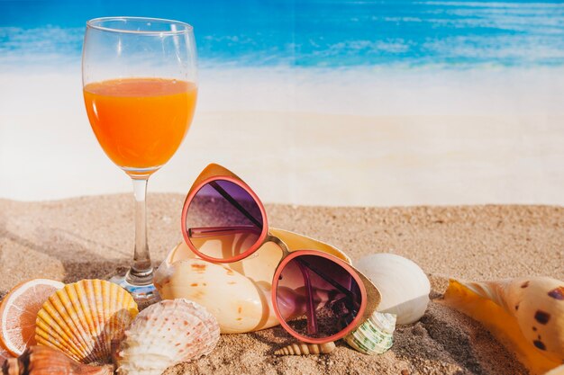 Composición veraniega con bebida, gafas de sol y conchas marinas