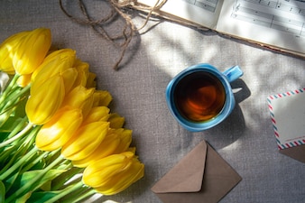 Composición vintage con una taza de té, tulipanes y notas planas.