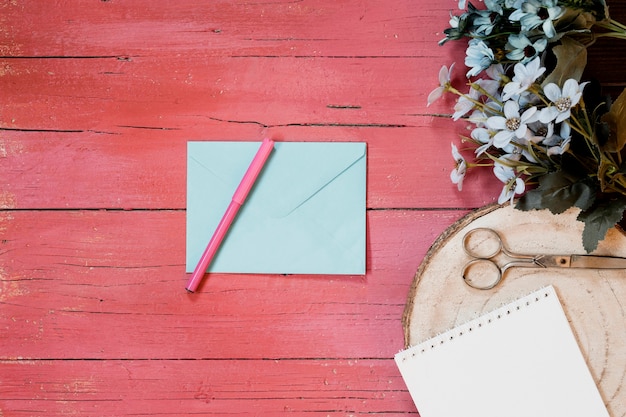 Composiciones de boda con sobre de invitación, flores, bolígrafo y tijeras sobre un fondo de madera rosa claro