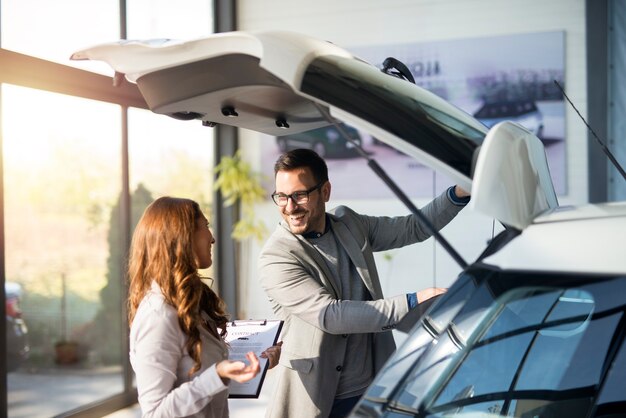 Comprador de automóviles probando el espacio del maletero de un automóvil nuevo en la sala de exposición del concesionario de vehículos local