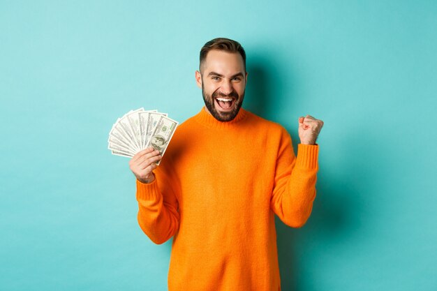 Compras. Chico alegre sosteniendo dinero, ganando un premio en efectivo y haciendo bomba de puño, triunfando