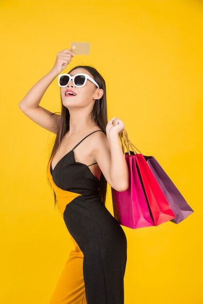 Compras hermosa mujer con gafas con una tarjeta de crédito de oro con una bolsa de papel de colores en un amarillo.