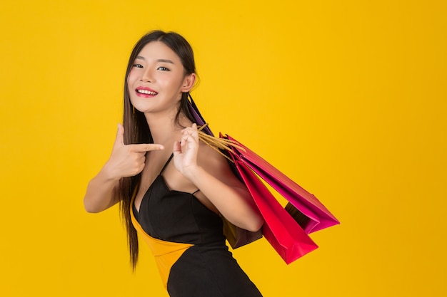 Compras hermosa mujer sosteniendo una bolsa de papel de colores en un amarillo.