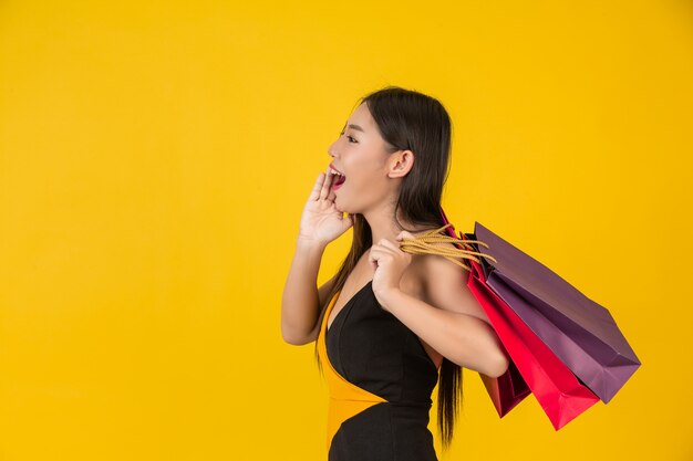 Compras hermosa mujer sosteniendo una bolsa de papel de colores en un amarillo.