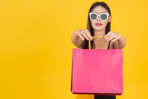 Compras de hermosas mujeres con gafas con bolsas de papel de colores sobre un fondo amarillo.