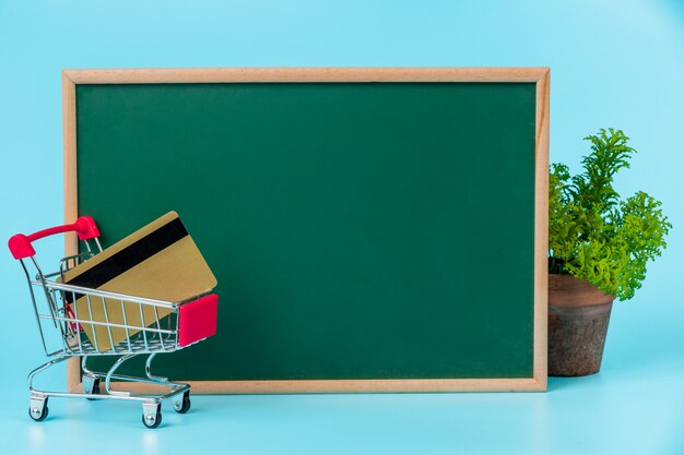 Compras en línea, un carrito doble colocado en un tablero verde sobre un azul.