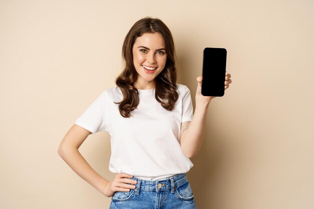 Compras en línea y concepto de aplicación mujer joven sonriendo y mostrando la aplicación de pantalla de teléfono móvil inter...