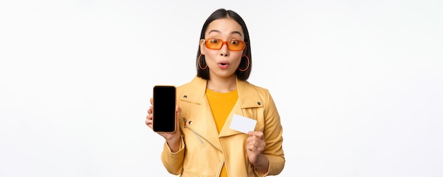 Compras en línea y concepto de personas elegante mujer asiática que muestra la pantalla del teléfono móvil y la tarjeta de crédito s