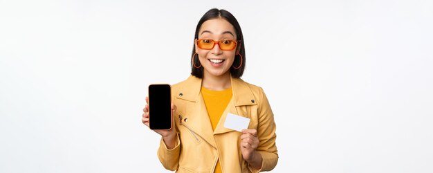 Compras en línea y concepto de personas elegante mujer asiática que muestra la pantalla del teléfono móvil y la tarjeta de crédito s