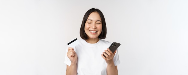 Compras en línea Mujer asiática feliz usando tarjeta de crédito y aplicación de teléfono inteligente pagando en el sitio web a través del fondo blanco del teléfono móvil