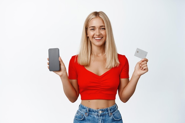 compras en línea, mujer rubia sonriente, actuación, pantalla del teléfono móvil, y, tarjeta de crédito, posición, contra, fondo blanco