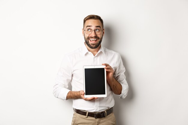 Compras y tecnología. Hombre pensativo que muestra la pantalla de la tableta digital, mirando la esquina superior izquierda y pensando, de pie