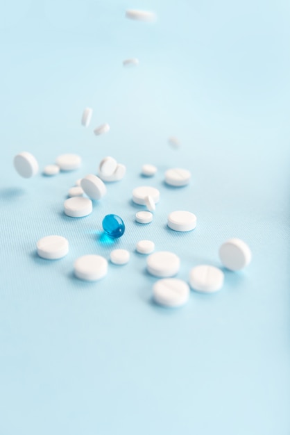 Comprimidos blancos caídos con una cápsula azul aislada