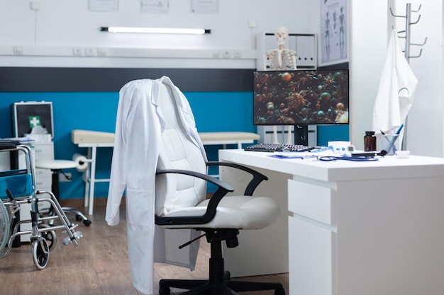 Computadora con ilustración covid19 en pantalla de pie en el escritorio en una sala de oficina vacía durante una pandemia mundial. Sala de hospital moderna equipada con instrumentos médicos profesionales. Imagen de célula de virus