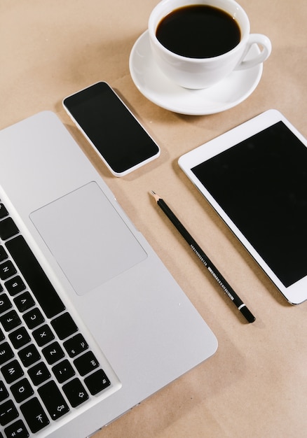 Computadora portátil, bloc de notas, tableta y una taza de café sobre la mesa