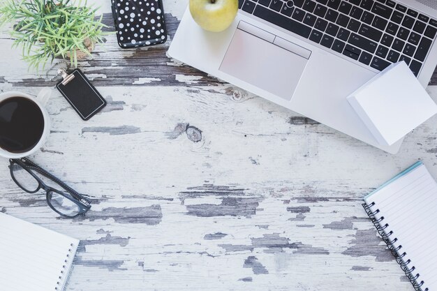 Computadora portátil y papelería cerca de una taza de café y vasos