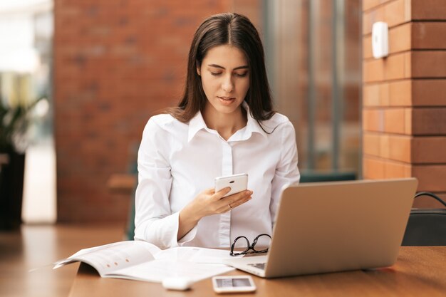 Comunicación corporativa. Empresaria caucásica hablando por teléfono móvil trabajando en equipo portátil en la oficina moderna.