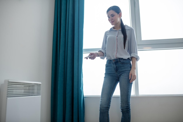 Concentrado joven hermosa mujer caucásica de pelo oscuro con un mando a distancia para calentar una sala de estar