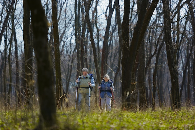 Concentrado y serio. Pareja de familia de hombre y mujer en traje de turista caminando en el césped cerca de árboles en un día soleado. Concepto de turismo, estilo de vida saludable, relajación y convivencia.