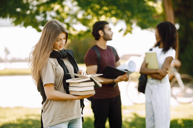 Concéntrese en una chica caucásica que está de pie por separado. Grupo de estudiantes internacionales parados juntos en el parque en la universidad