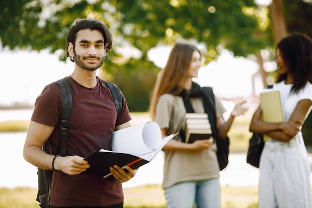 Concéntrese en un niño indio que está parado por separado. Grupo de estudiantes internacionales parados juntos en el parque en la universidad