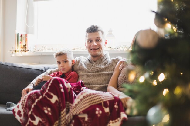 Concept de navidad con familia sentada en sofá al lado de árbol de navidad