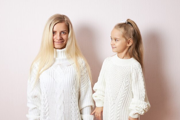 Concepto de amor, familia, cuidado y relaciones. Elegante mujer joven con cabello largo rubio disfrutando de dulces momentos de maternidad posando con su curiosa y juguetona hijita