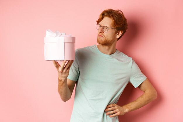 Concepto de amor y vacaciones intrigado chico pelirrojo mirando desconcertado en caja de regalo no sé qué dentro de st ...