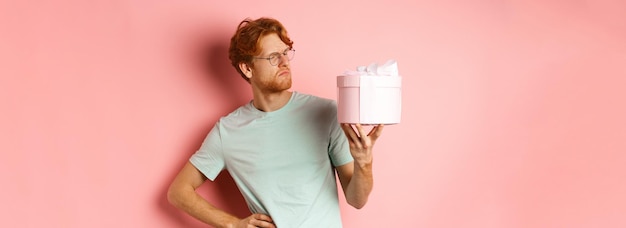 Foto gratuita el concepto de amor y vacaciones intrigó al chico pelirrojo mirando desconcertado a la caja de regalo no sé qué dentro de st