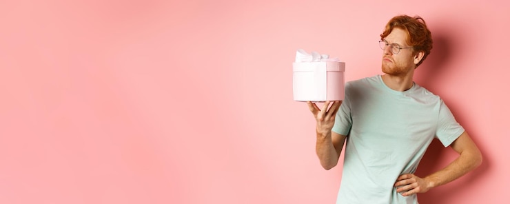 Foto gratuito el concepto de amor y vacaciones intrigó al chico pelirrojo mirando desconcertado a la caja de regalo no sé qué dentro de st