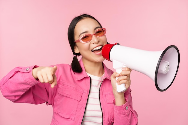 Concepto de anuncio de atención Chica asiática entusiasta gritando en publicidad de megáfono con reclutamiento de oradores de pie sobre fondo rosa