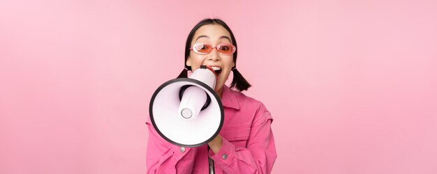 Concepto de anuncio de atención Chica asiática entusiasta gritando en publicidad de megáfono con reclutamiento de oradores de pie sobre fondo rosa