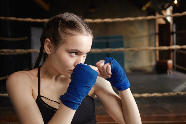 Concepto de artes marciales, boxeo, kickboxing y entrenamiento. Close Up retrato de hermosa adolescente haciendo ejercicio en el interior, vistiendo vendas